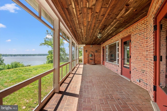 unfurnished sunroom with a water view, wood ceiling, brick floors, and brick wall