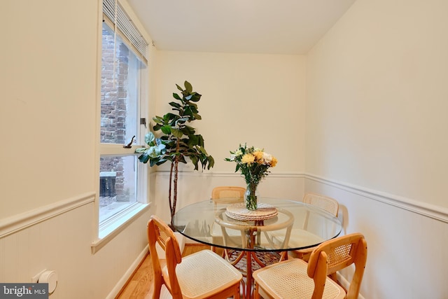 dining space featuring healthy amount of natural light, wood finished floors, and a wainscoted wall