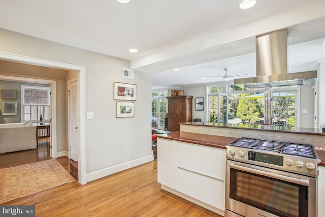 kitchen with light wood finished floors, stainless steel gas range oven, white cabinetry, baseboards, and recessed lighting
