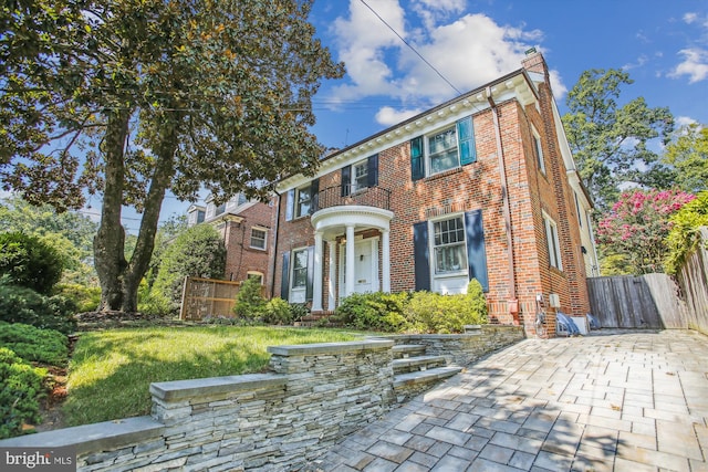 view of front of property with a chimney, brick siding, fence, a patio area, and a front lawn