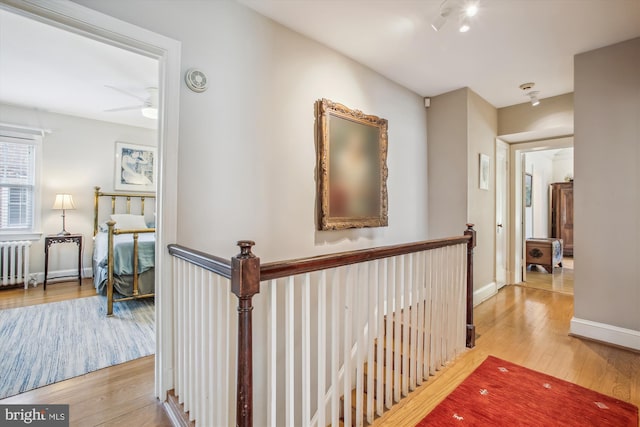 hallway with radiator, wood finished floors, an upstairs landing, and baseboards