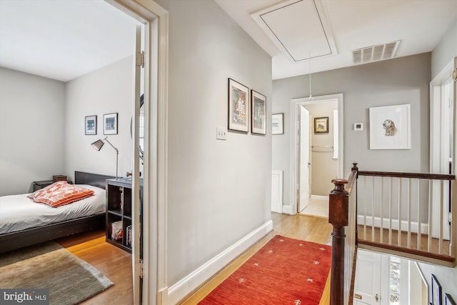 hallway featuring wood finished floors, attic access, an upstairs landing, visible vents, and baseboards