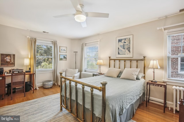 bedroom featuring wood finished floors, baseboards, multiple windows, and radiator heating unit