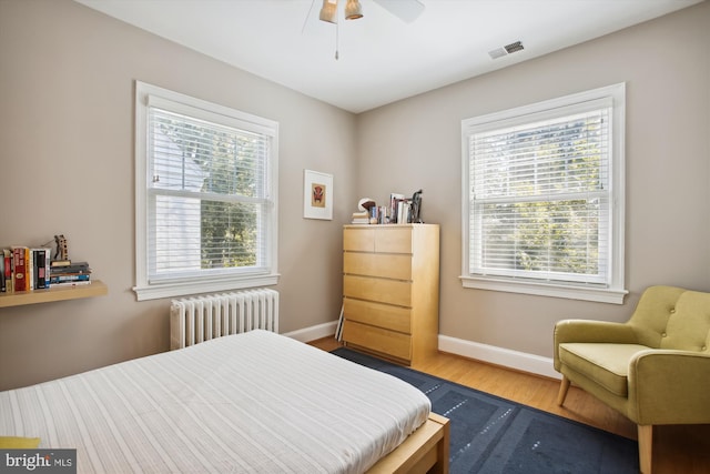 bedroom with radiator, baseboards, multiple windows, and wood finished floors