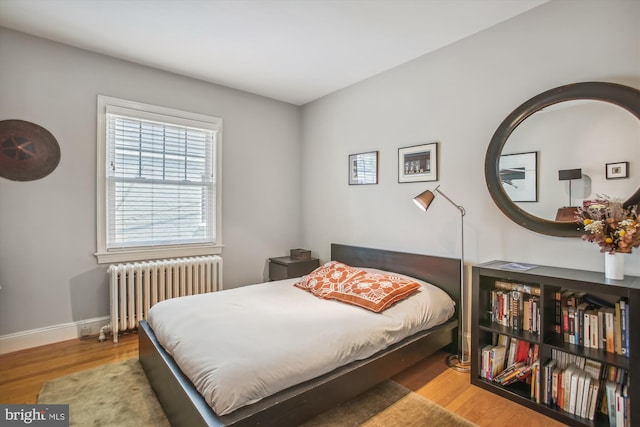 bedroom featuring baseboards, radiator heating unit, and wood finished floors