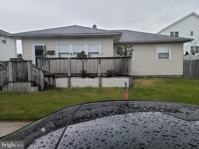 rear view of property with a lawn, roof with shingles, and a deck