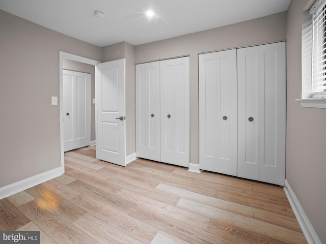unfurnished bedroom featuring two closets, baseboards, and wood finished floors