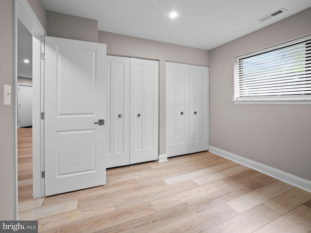 unfurnished bedroom featuring two closets, visible vents, baseboards, light wood-type flooring, and recessed lighting