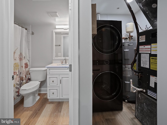 full bathroom with toilet, wood finished floors, stacked washer and dryer, water heater, and vanity