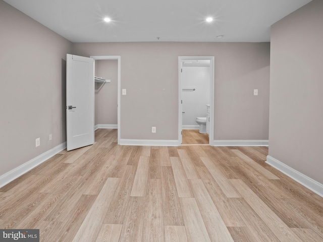 unfurnished bedroom featuring a walk in closet, light wood-style flooring, baseboards, and recessed lighting