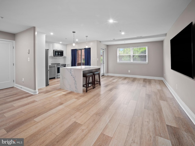 kitchen featuring stainless steel appliances, a breakfast bar area, recessed lighting, light wood-style flooring, and open floor plan