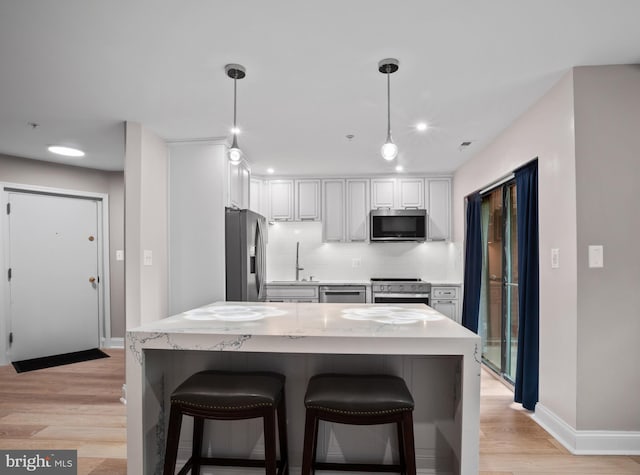 kitchen featuring light wood-style flooring, pendant lighting, baseboards, backsplash, and appliances with stainless steel finishes