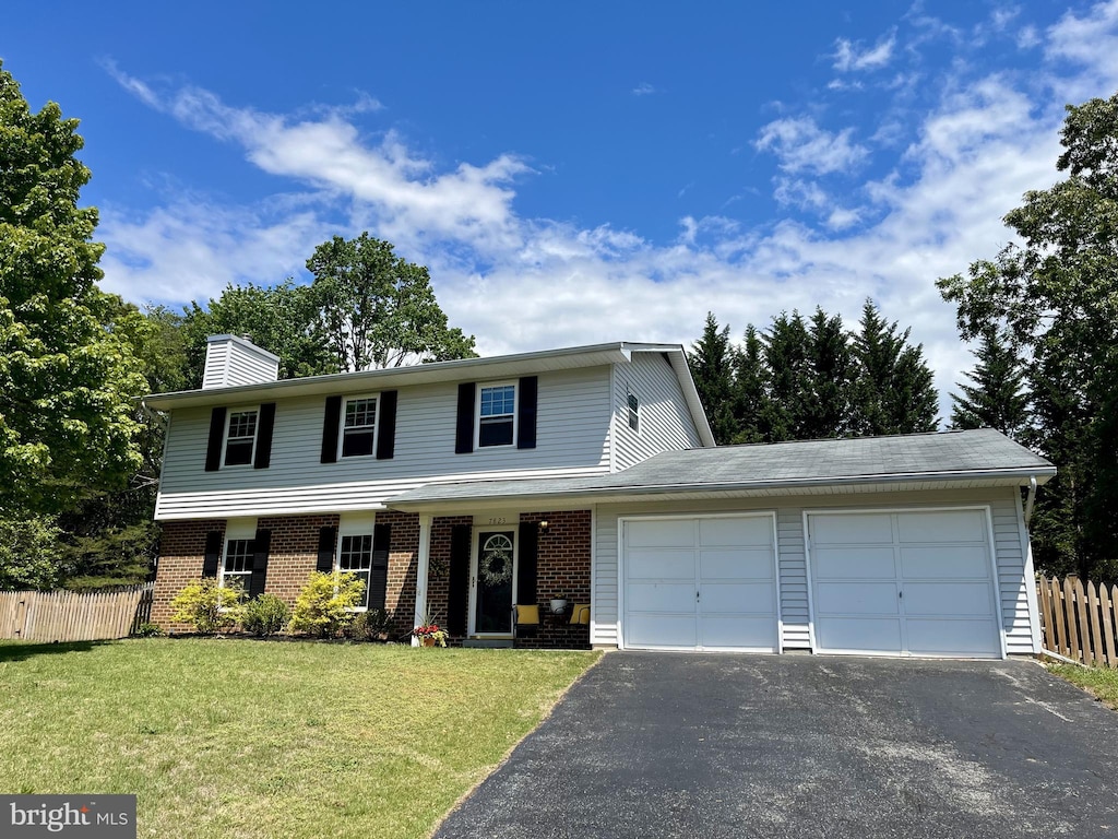 traditional-style house featuring a garage, fence, a front yard, brick siding, and driveway