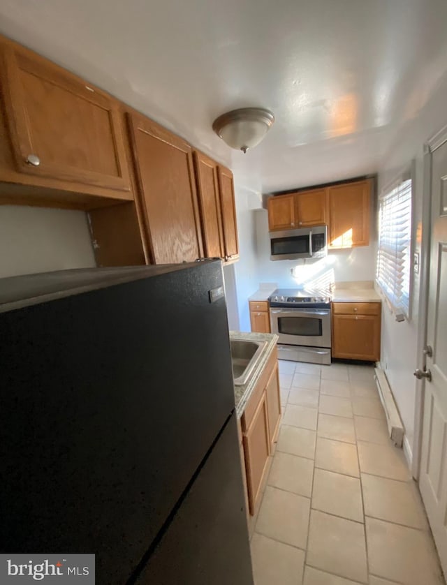 2718 W Sterner St, Philadelphia, PA 19132 - kitchen featuring a sink, brown cabinetry, a baseboard heating unit, light tile patterned flooring, and appliances with stainless steel finishes