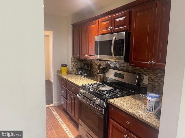 kitchen featuring baseboards, appliances with stainless steel finishes, decorative backsplash, and light stone countertops