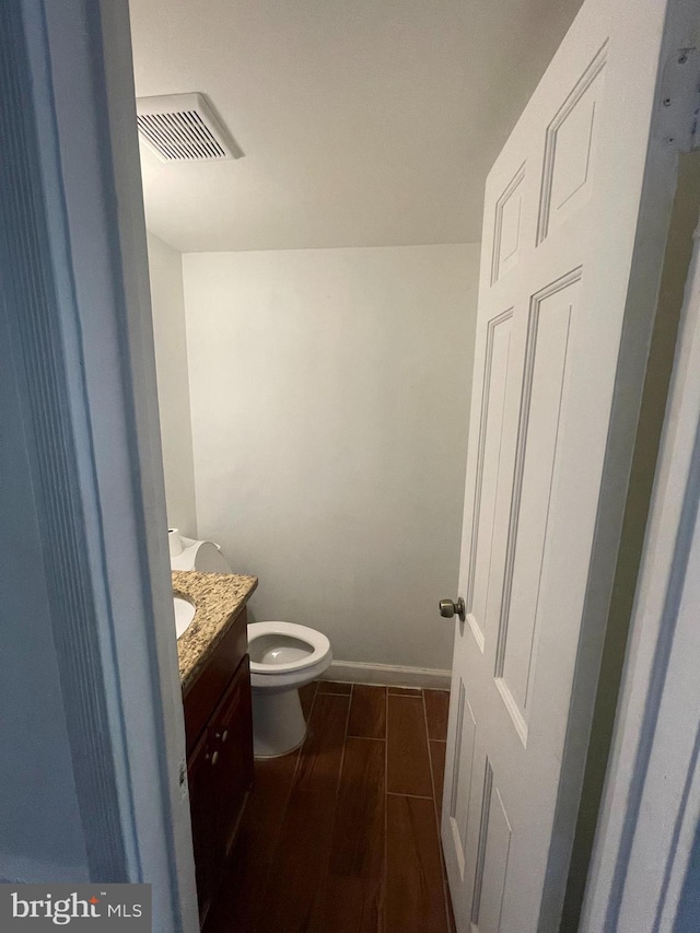 half bathroom with vanity, toilet, baseboards, wood finished floors, and visible vents