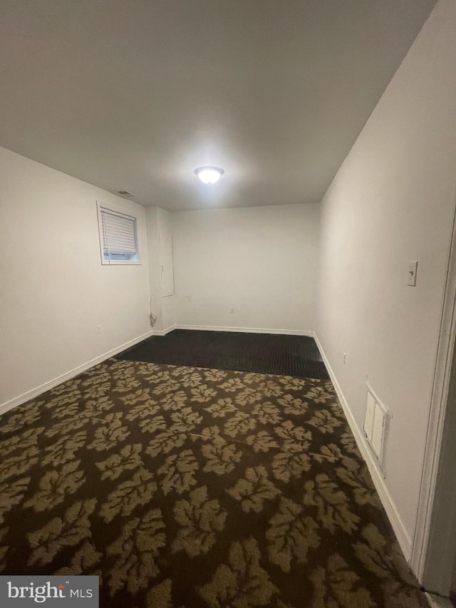 finished below grade area featuring baseboards, visible vents, and dark carpet