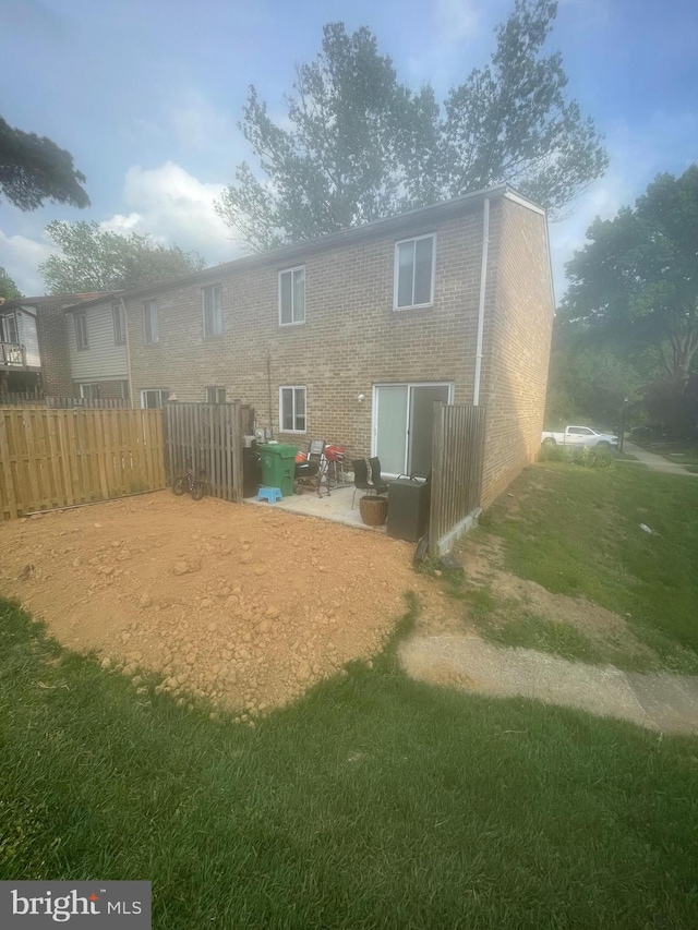 rear view of property with brick siding, a patio area, fence, and a yard