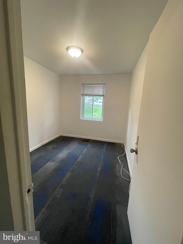unfurnished room featuring baseboards and dark colored carpet
