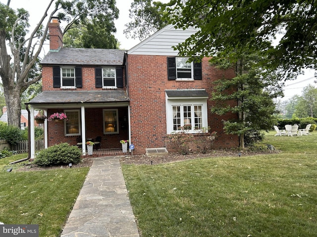 traditional-style home featuring a chimney, a front yard, a porch, brick siding, and a high end roof