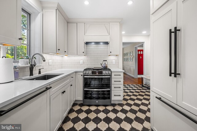kitchen featuring double oven range, a sink, dark floors, custom range hood, and dishwasher