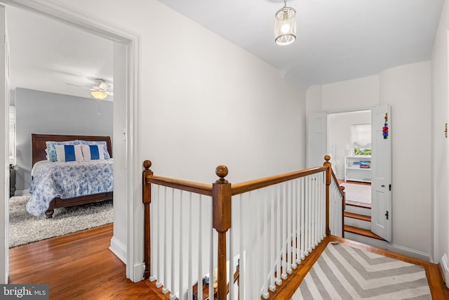 corridor featuring wood finished floors, an upstairs landing, and baseboards