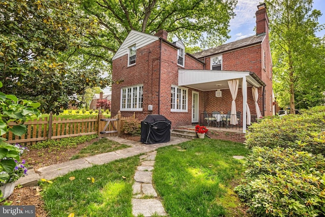 back of property featuring a chimney, brick siding, fence, and covered porch