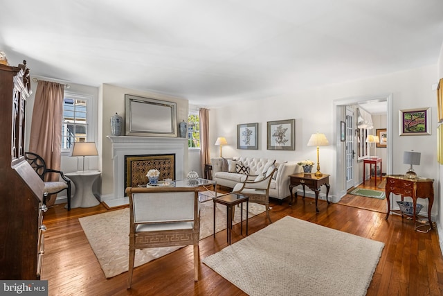 living area featuring plenty of natural light, a fireplace with raised hearth, hardwood / wood-style floors, and baseboards