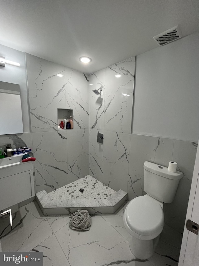 full bathroom with vanity, toilet, a marble finish shower, marble finish floor, and tile walls