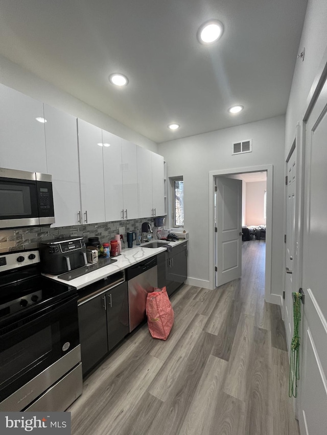 kitchen featuring decorative backsplash, visible vents, appliances with stainless steel finishes, a sink, and white cabinets