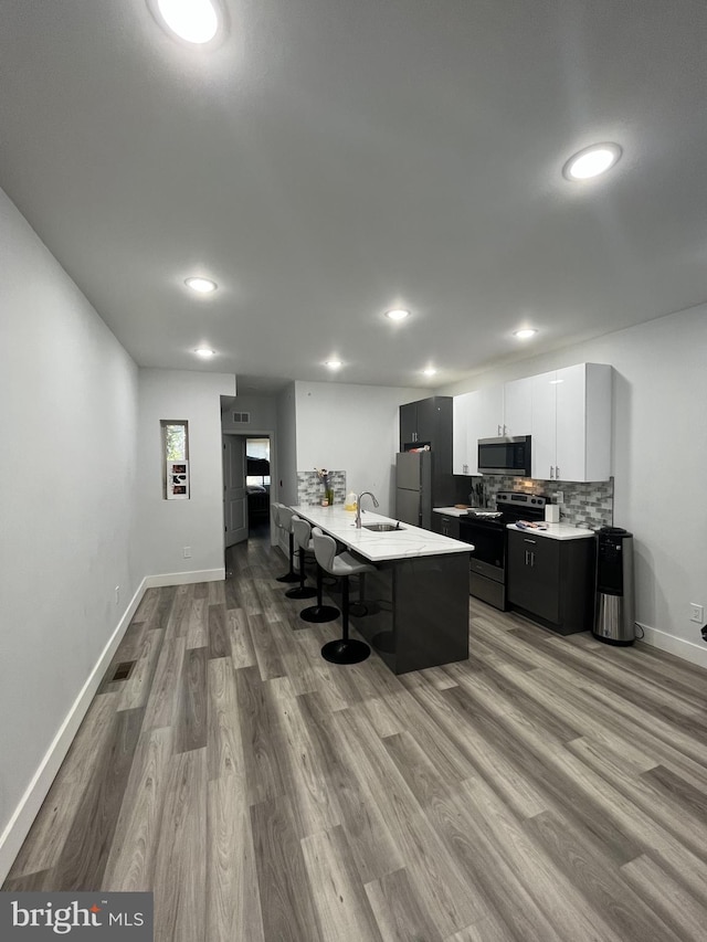 kitchen with a sink, light countertops, stainless steel appliances, wood finished floors, and a kitchen bar