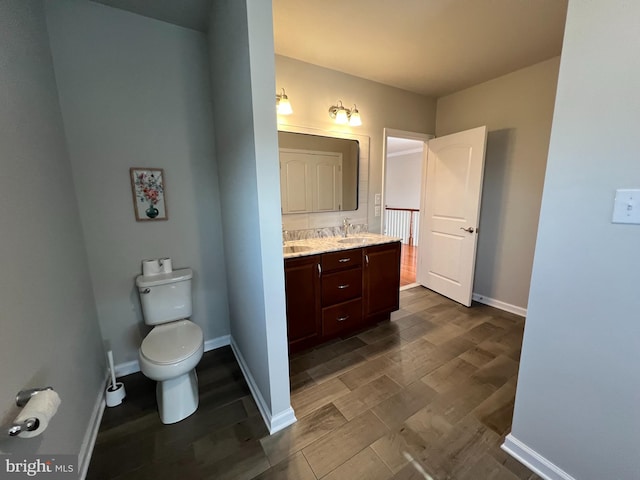 bathroom featuring double vanity, wood finished floors, a sink, baseboards, and toilet
