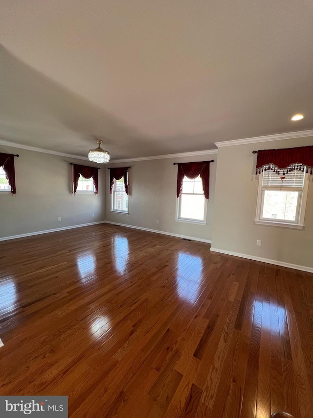 unfurnished living room featuring an inviting chandelier, ornamental molding, baseboards, and wood finished floors