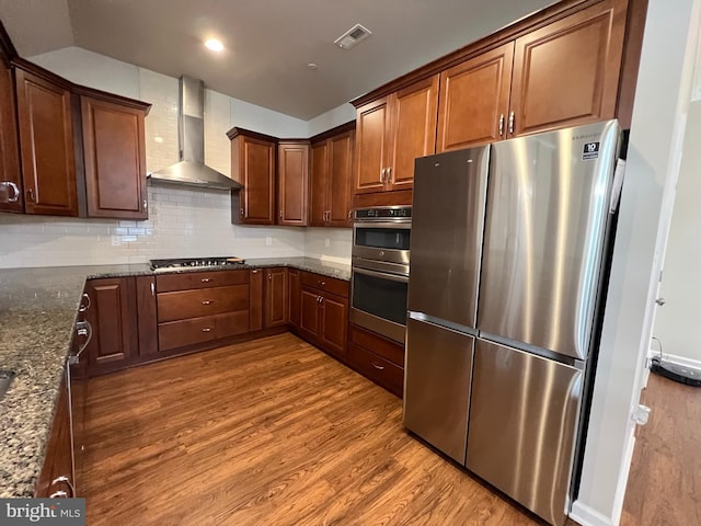 kitchen with visible vents, dark wood-style floors, wall chimney range hood, dark stone countertops, and appliances with stainless steel finishes