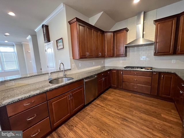 kitchen featuring wood finished floors, stone countertops, wall chimney range hood, a sink, and stainless steel appliances