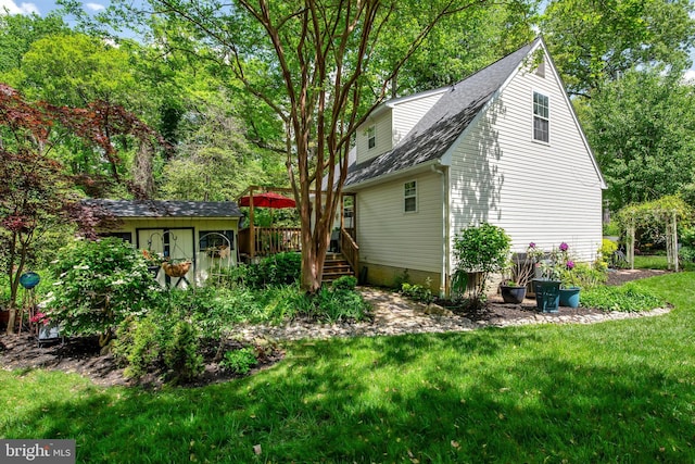back of house with an outdoor structure, a lawn, roof with shingles, and a storage unit
