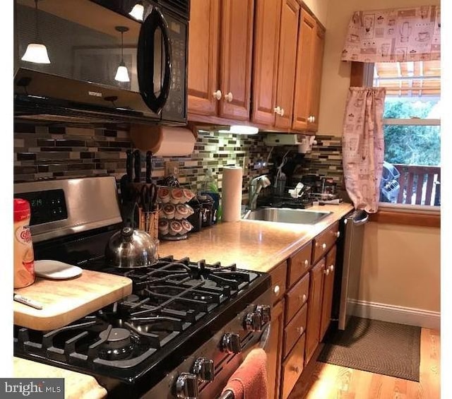 kitchen with brown cabinetry, black microwave, gas stove, light countertops, and a sink