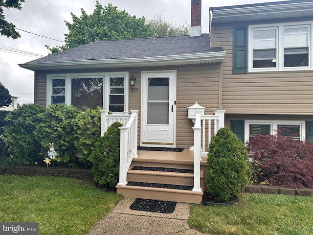 doorway to property with roof with shingles, a chimney, and a lawn
