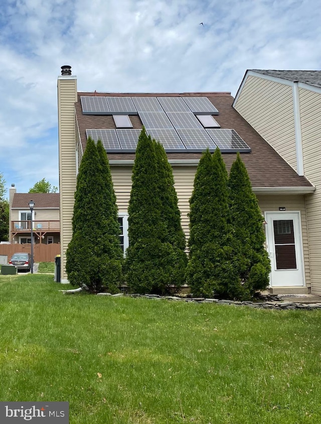 view of side of property featuring roof mounted solar panels, roof with shingles, a yard, and a chimney