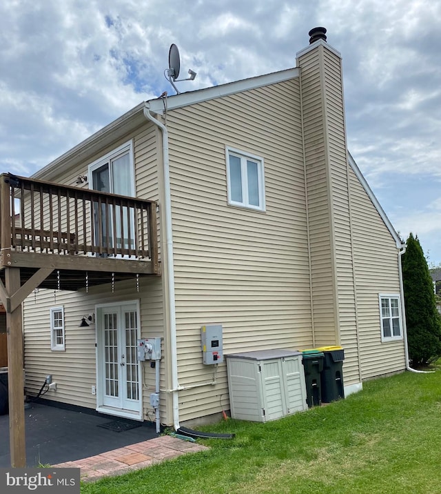 rear view of property with french doors, a chimney, a lawn, a wooden deck, and a patio