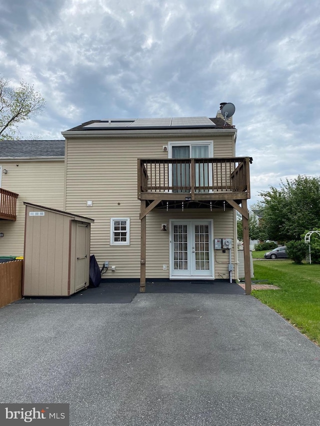 back of house with french doors, solar panels, a wooden deck, a storage unit, and a yard