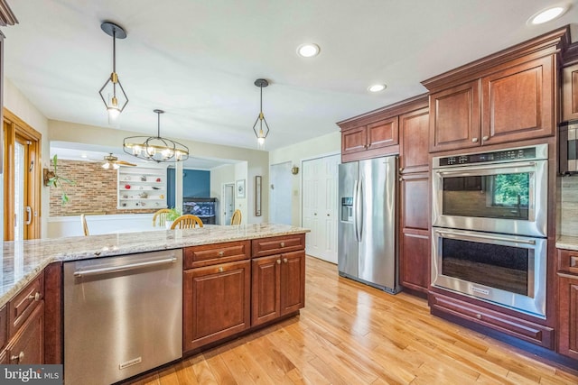 kitchen featuring stainless steel appliances, light wood finished floors, hanging light fixtures, a chandelier, and light stone counters