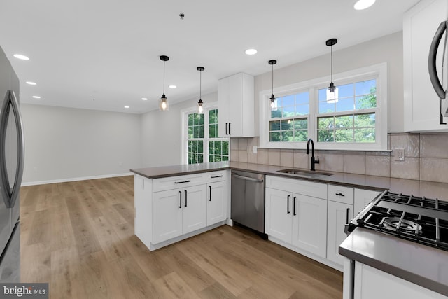 kitchen featuring a sink, a peninsula, appliances with stainless steel finishes, dark countertops, and light wood-style floors