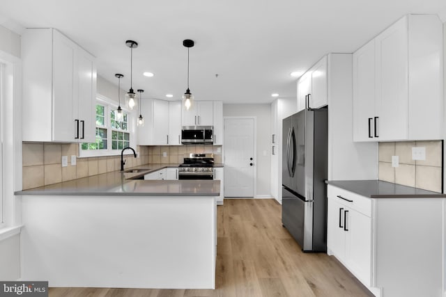 kitchen with a sink, white cabinets, light wood-style floors, stainless steel appliances, and tasteful backsplash