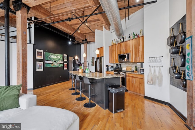 kitchen with stainless steel appliances, light wood-style flooring, a towering ceiling, and brown cabinets