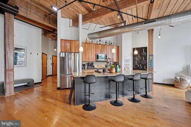 kitchen with appliances with stainless steel finishes, brown cabinets, a towering ceiling, and wood ceiling