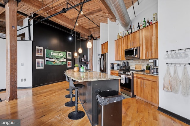 kitchen featuring appliances with stainless steel finishes, a kitchen island, brown cabinets, and a high ceiling
