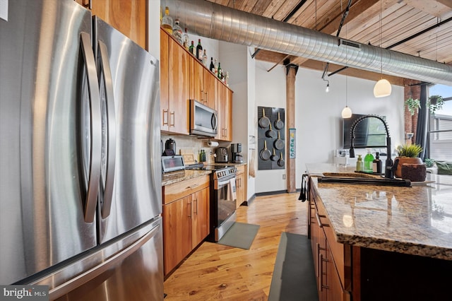 kitchen with light wood-type flooring, brown cabinets, pendant lighting, and appliances with stainless steel finishes