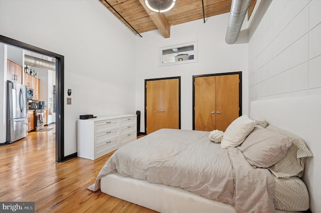 bedroom with light wood finished floors, wood ceiling, high vaulted ceiling, freestanding refrigerator, and beamed ceiling