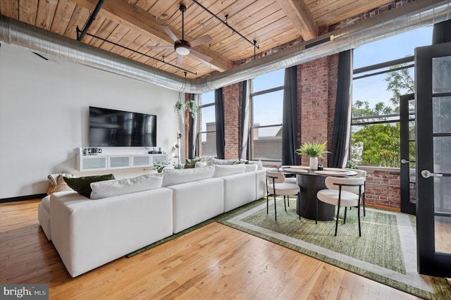 living area featuring wood finished floors, beamed ceiling, a ceiling fan, brick wall, and wood ceiling